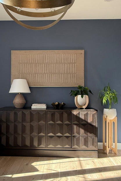 Modern interior with a dark wooden sideboard, decorative lamp, and the Nested &amp; Arches Plant stands against a blue wall.
