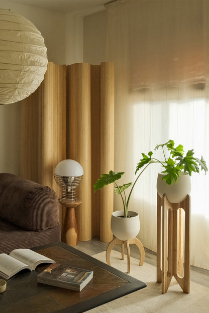 Modern living room with a brown sofa, white ceiling lamp and the Arches &amp; Nested Plant Stands with houseplants next to a large window. 