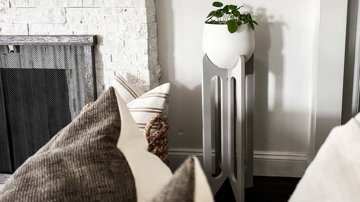 Kandis Cottage tall plant stand in gray with white pot and houseplant next to fireplace