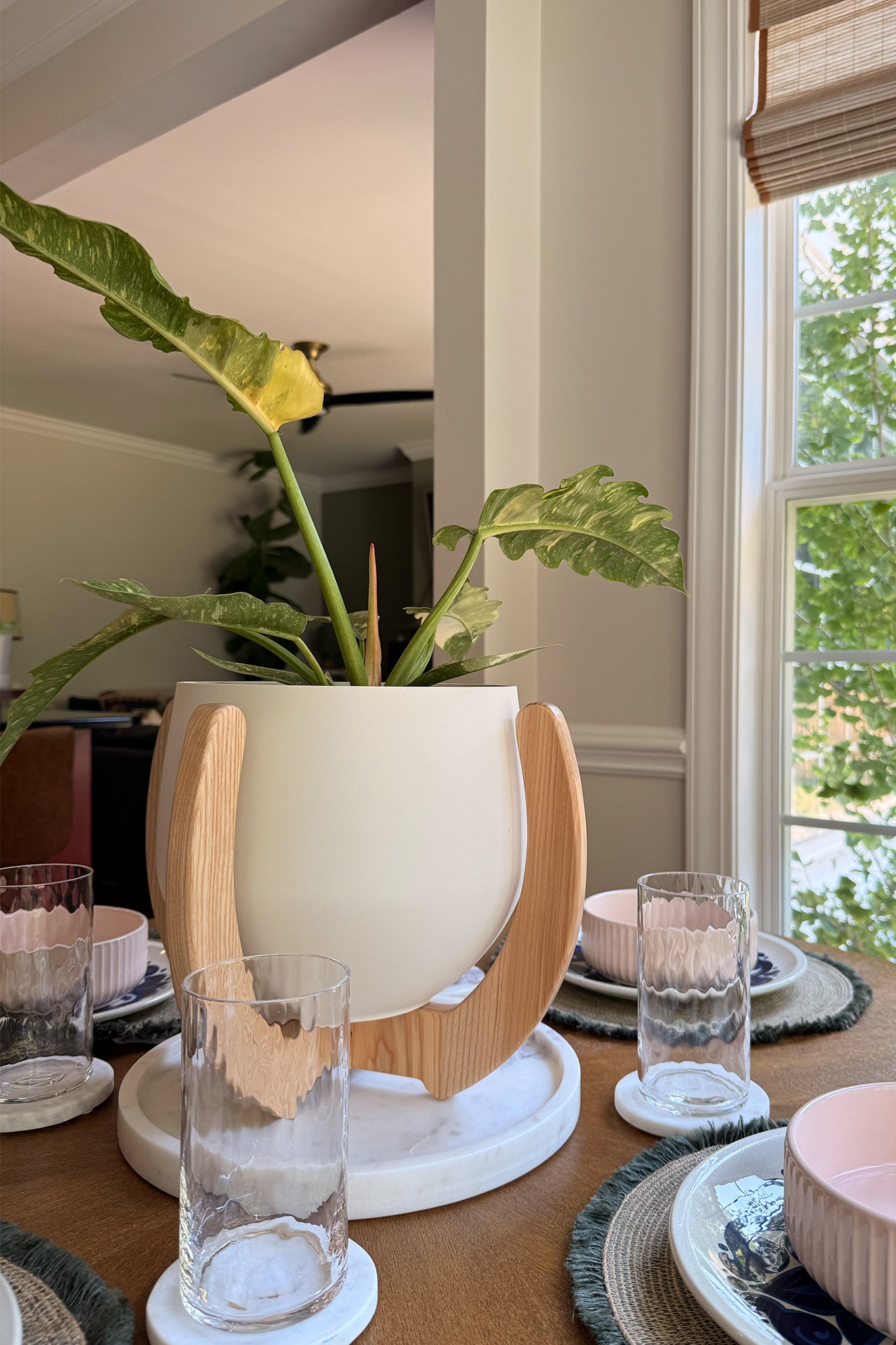 The Nested Plant Stand with a houseplant on a wooden dining table, complete with dinner service.