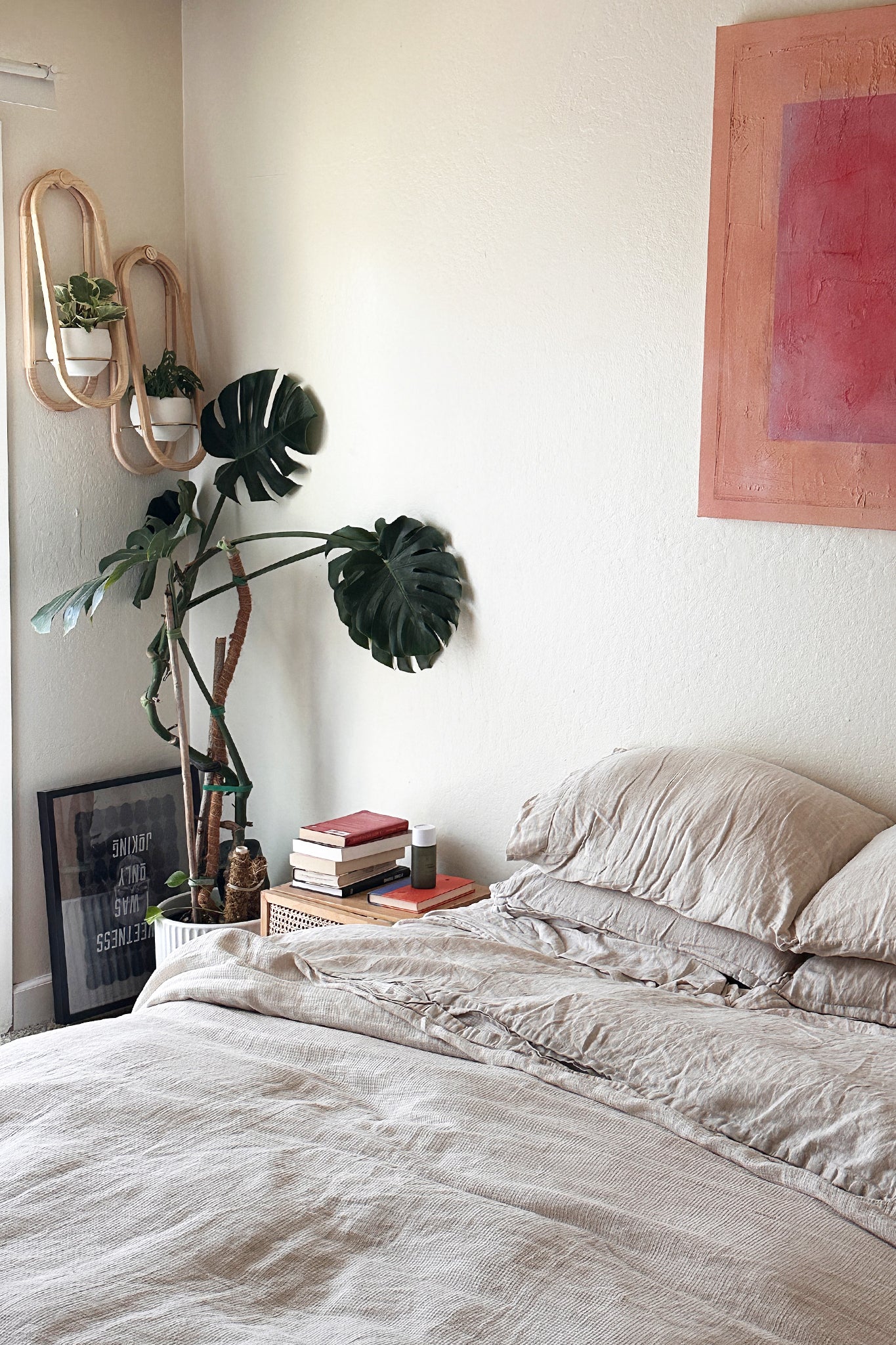 A modern bedroom with a taupe bedspread, red & orange artwork, houseplants, and two Frame Wall Planters on the wall.