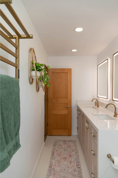 A clean and modern bathroom with white countertops, a pink rug, a green towel, and two Frame Wall Planters on the wall. 