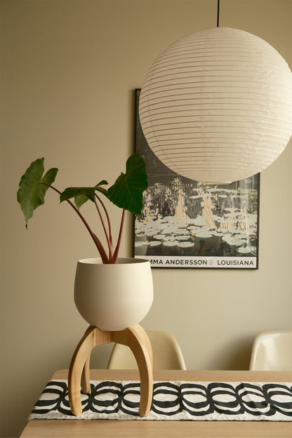 White lampshade hanging above a table with a Nested Plant Stand on the table.
