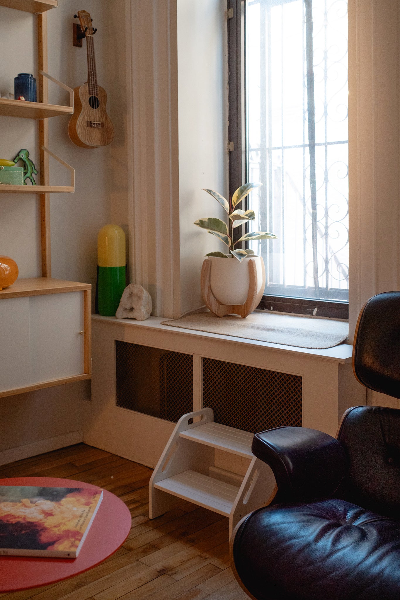 A room with tall bookcases filled with decorative elements, a black armchair, and a Nested Plant Stand on the window seat.