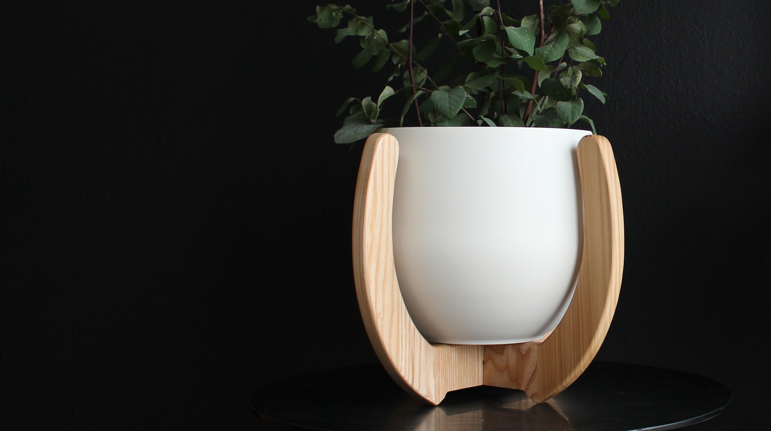 modern nested hardwood plant stand on a black table against a black wall