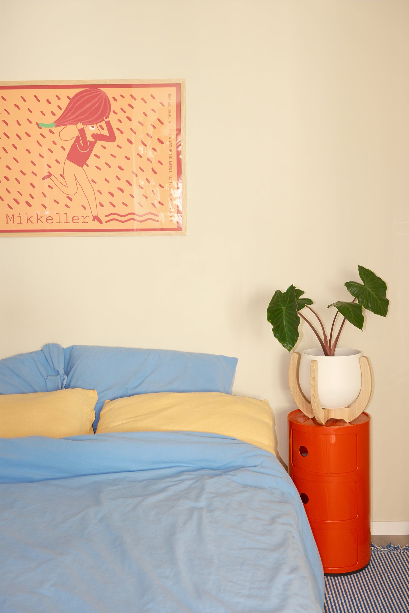Bedroom with blue bedding, yellow pillows, and the Nested Plant Stand on an orange side table.