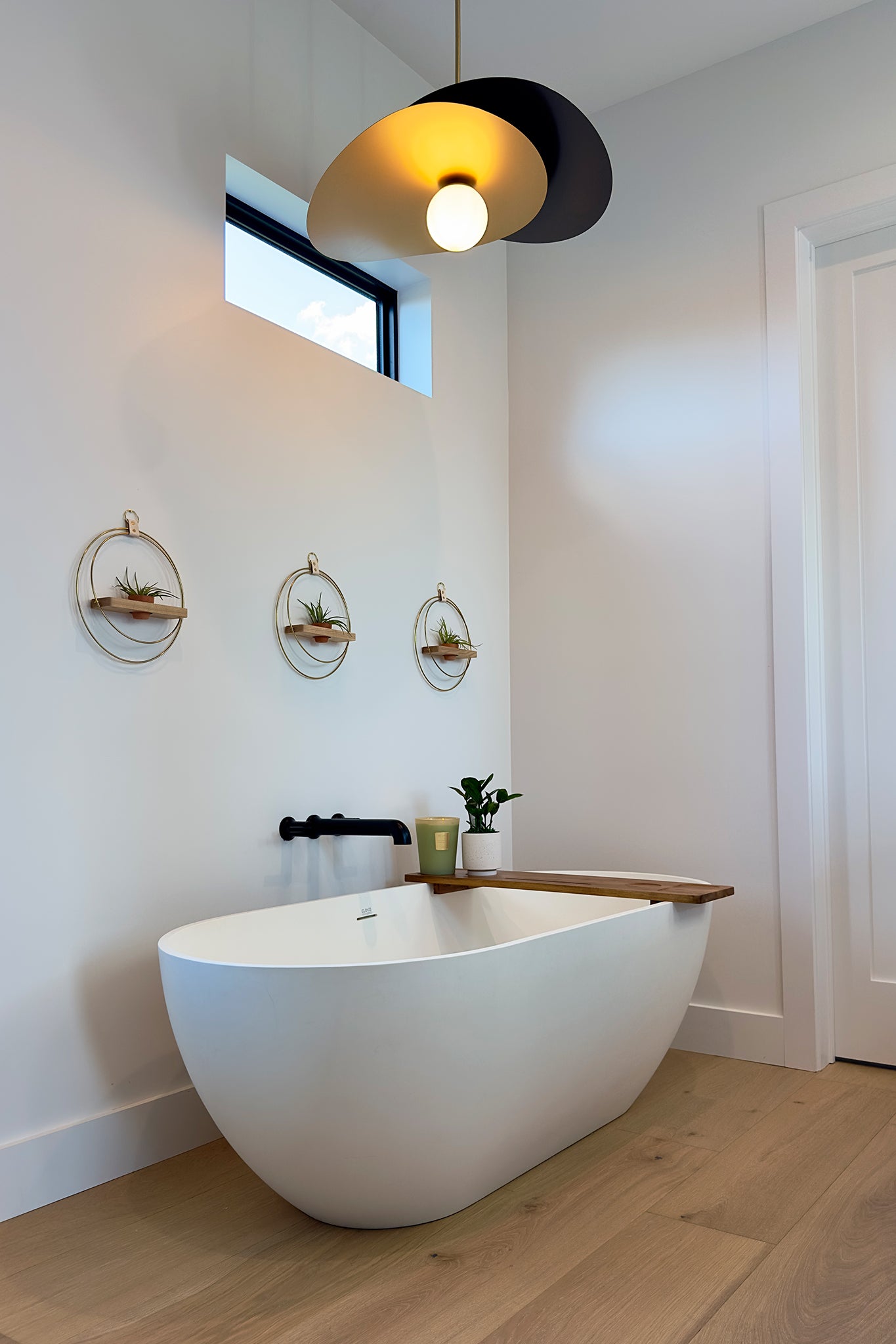Modern bathroom with a freestanding bathtub, pendant light, and wall-mounted circular planters with air plants.